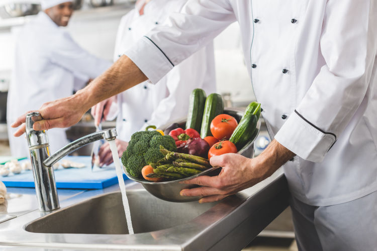Chef washing fresh vegetables as part of food safety training in kitchen