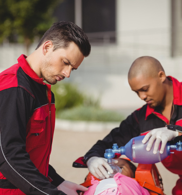 Two paramedics administering oxygen to a patient during a medical emergency in an outdoor setting.