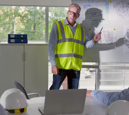 Construction manager in a reflective vest conducting a safety training meeting with engineers, using site plans and diagrams.