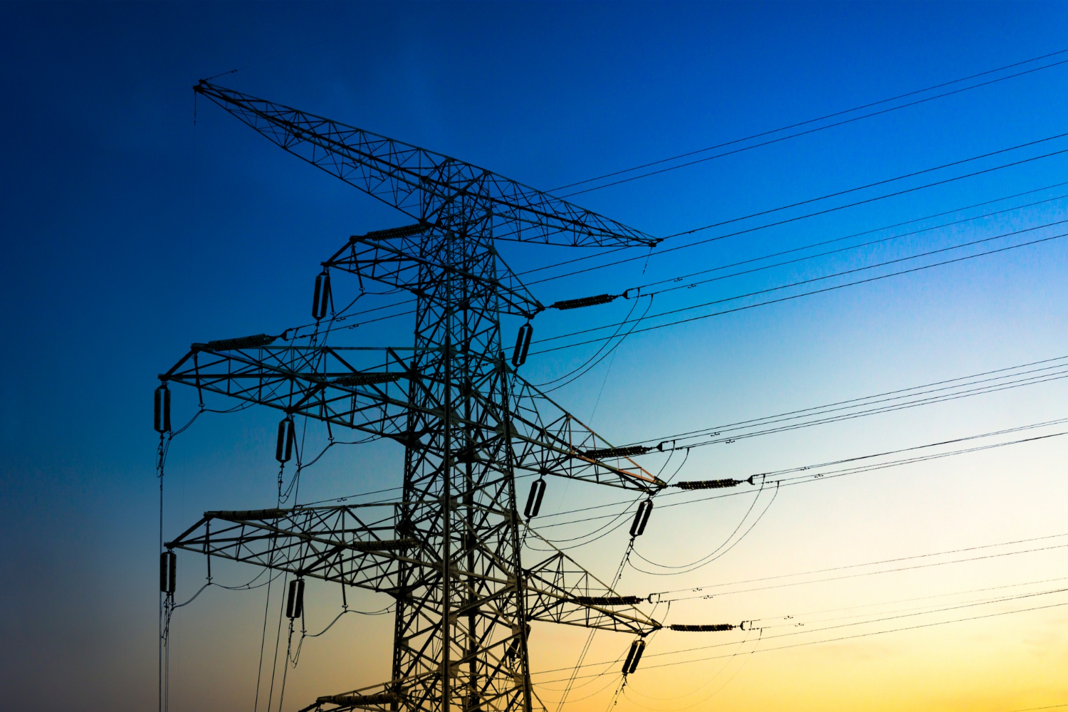 Power transmission tower silhouetted against a gradient sunset sky, symbolizing energy infrastructure and safety in the power industry.