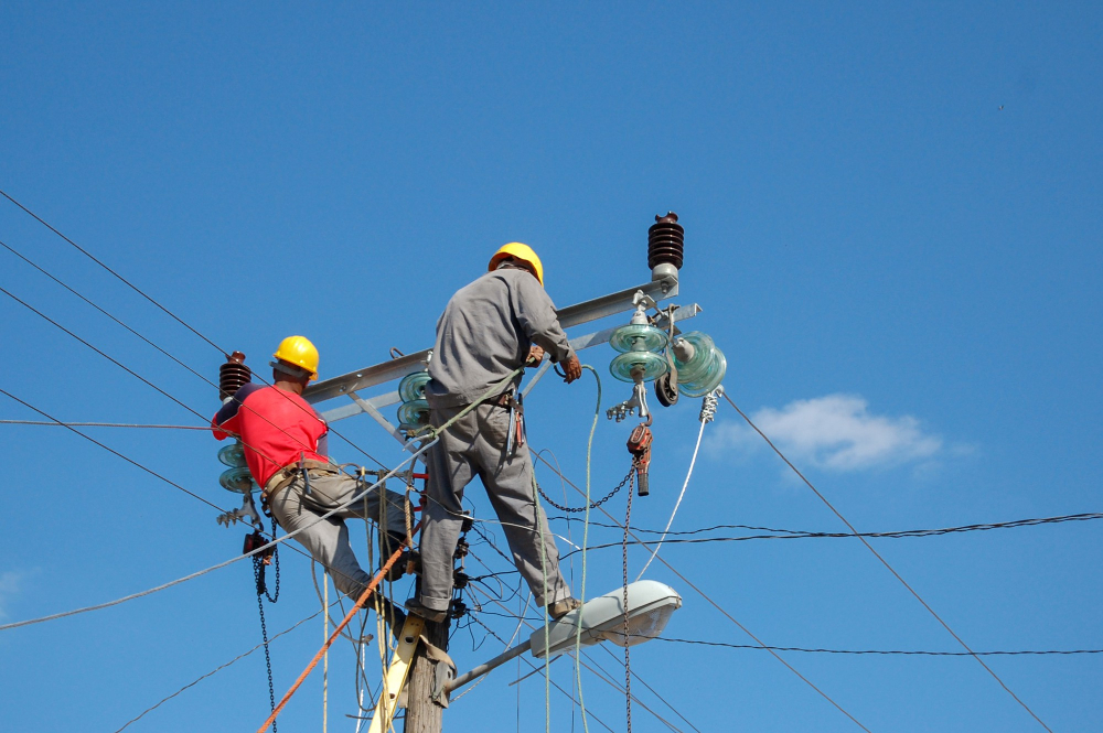 Two utility workers in hard hats performing maintenance on power lines, emphasizing safety and teamwork in the energy sector.