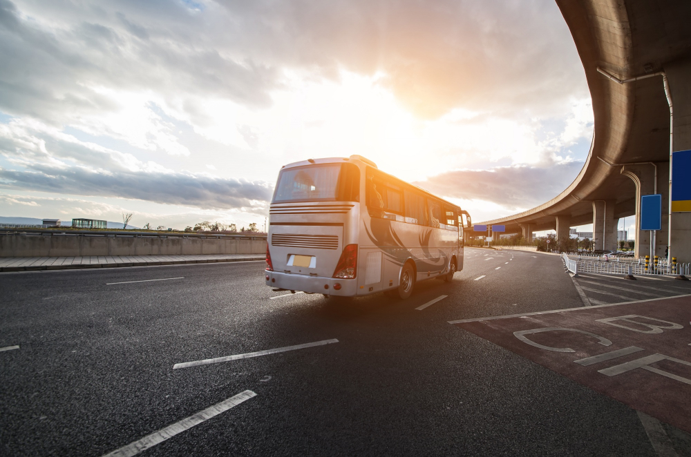 White passenger bus traveling on urban expressway during sunrise.