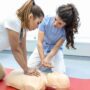 Two women practicing CPR techniques on a training dummy during a certified CPR training course, emphasizing first aid skills and emergency preparedness.
